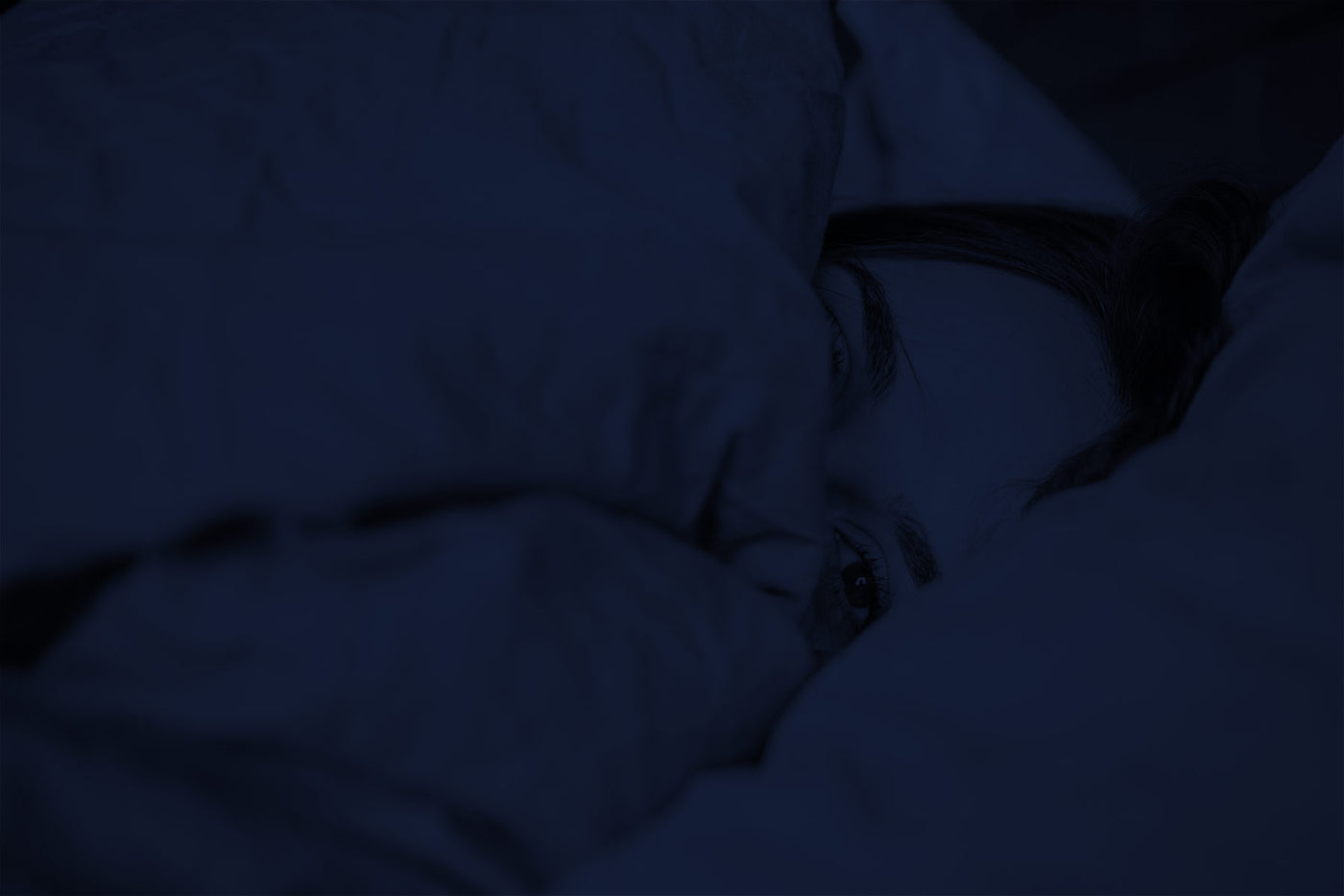 Gerade aufgewachte Frau im Bett eingekuschelt in Bettdecke